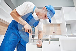 Kitchen installation. Worker assembling furniture