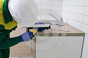 The kitchen installer holds a gun with silicone and smears the end of the countertop to protect it from moisture