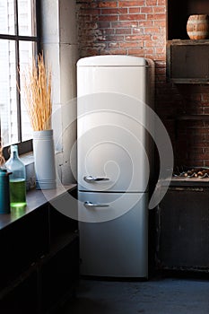 Kitchen interior in dark textured colors with white modern retro fridge, rustic brick wall, window and vase decor