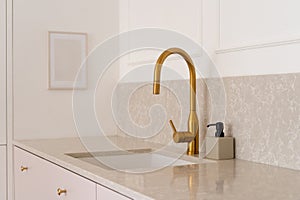 Kitchen interior with golden faucet and sink built into marble countertop