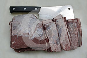 Kitchen knife and beef meat cut into big slices on white cutting board.
