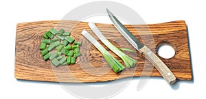 Kitchen knife and chopped spring green onion stems on wooden chopping board isolated
