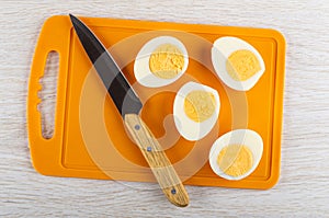 Knife, halves of peeled eggs on cutting board on wooden table. Top view