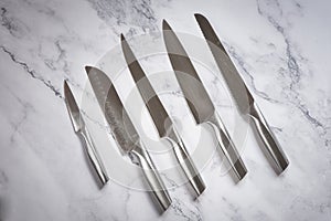 Kitchen knives set made of steel on marble table. High angle view