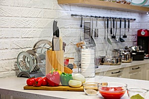 Kitchen knives in a special wooden stand with spice jars and fresh vegetables lie on a wooden board. Close-up. Kitchen