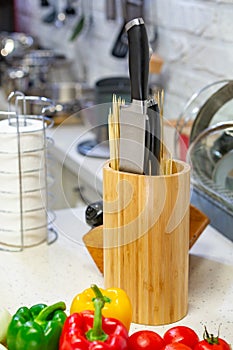 Kitchen knives in a special wooden stand with spice jars and fresh vegetables lie on a wooden board. Close-up. Kitchen