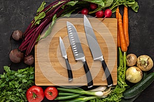 Kitchen Knives on Wooden Chopping Board with Fresh Vegetables Background. Vegetarian Raw Food.