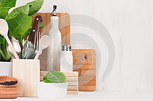 Kitchen modern decor - beige wooden utensils, brown cutting boards, green plant on soft light white wood background.