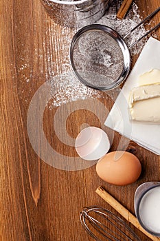Kitchen, pastry inventory lies on the wooden table. Butter, eggs, wooden spoons, whisk, flour, milk. Top view with copy space,