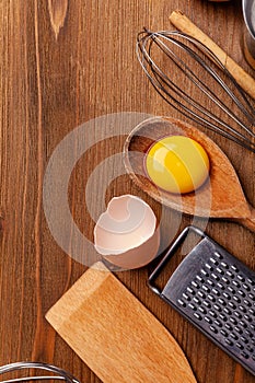 Kitchen, pastry inventory lies on the wooden table. Butter, eggs, wooden spoons, whisk, flour, milk. Top view with copy space