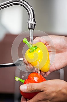 Kitchen porter washing red and yellow pepper under running tap