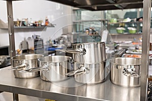 kitchen pots, grater, bowls, saucepans stacked up on a shelf in a kitchen; restaurant / commercial or home kitchen. Brick wall in