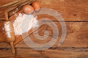 Kitchen rolling pin, wooden board with flour on wooden background, ears and eggs for making bread on table