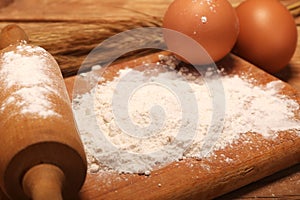 Kitchen rolling pin, wooden board with flour on wooden background, ears and eggs for making bread on table