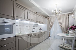 Kitchen room interior with white marble floor, countertops with built in cooker and comfortable wooden cupboards