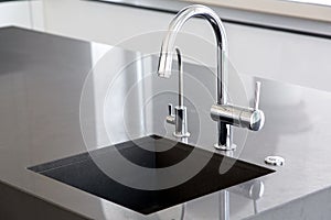 Kitchen sink of dark gray stone with chrome faucet.