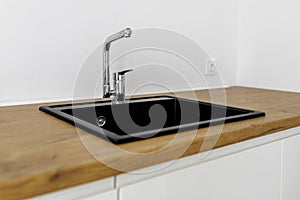 kitchen sink of dark gray stone with chrome faucet in a clean kitchen with a wooden work surface, close up faucet sink