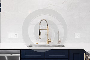 A kitchen sink detail with a gold faucet and blue cabinets.