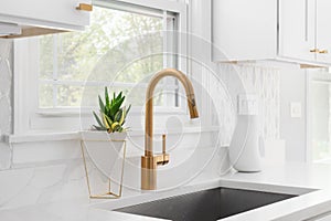 A kitchen sink detail with a gold faucet and marble tiled backsplash.