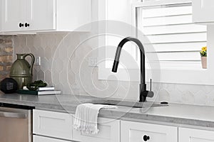 A kitchen sink detail with a marble countertop and hexagon tiled backsplash.