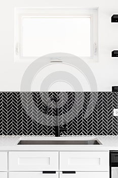 A kitchen sink detail shot with a black faucet and herringbone backsplash.