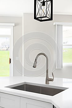 A kitchen sink detail with a white cabinet and black light fixture above.