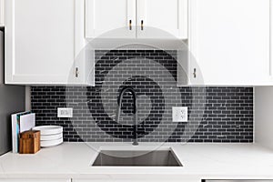 Kitchen sink detail with white cabinets and a black tile backsplash.