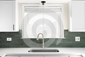 A kitchen sink detail in a white kitchen with green subway tile backsplash.