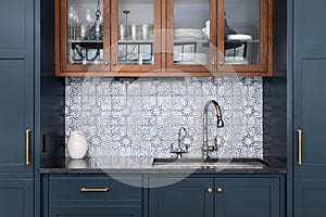 A kitchen sink surrounded by blue cabinets and a mosaic tile backsplash.