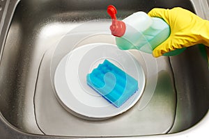 Kitchen sink with water, plate, blue cleaning sponge, detergent