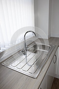 Kitchen sink by window with white vertical blinds.