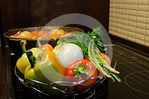 Kitchen still-life. Fresh raw vegetables and a boiling cauldron with appetizing supper meal on the electric stove. Fresh vegetable
