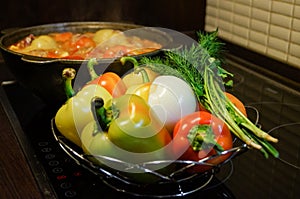 Kitchen still-life. Fresh raw vegetables and a boiling cauldron with appetizing supper meal on the electric stove. Fresh vegetable