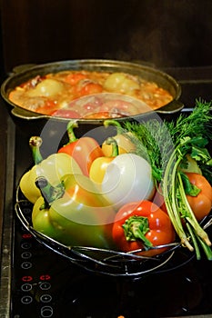 Kitchen still-life. Fresh raw vegetables and a boiling cauldron with appetizing supper meal on the electric stove. Fresh vegetable