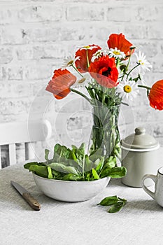 Kitchen still life - fresh spinach in a bowl, bouquet of poppies on the table in a bright room. Cozy interior home still life