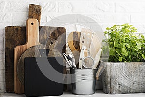 Kitchen still life on a white brick wall background: various cutting boards, tools, greens for cooking, fresh vegetables