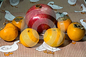 Kitchen still-life. Wholesome ripe fruits of pomegranate, mandarine and persimmon on a cute tablecloth.