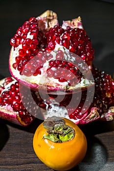 Kitchen still-life. Wholesome ripe fruits of pomegranate and persimmon on a dark brown table.