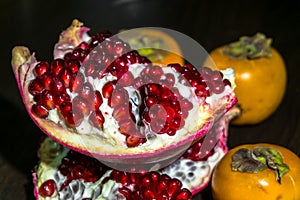 Kitchen still-life. Wholesome ripe fruits of pomegranate and persimmon on a dark brown table.