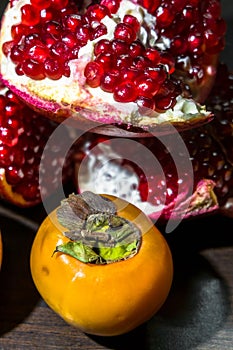 Kitchen still-life. Wholesome ripe fruits of pomegranate and persimmon on a dark brown table.