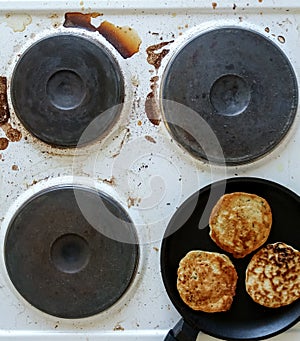 Kitchen stove dirty with burnt food and cooking oil, frying pan with pancakes on top