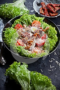 Kitchen table with green salad, bowls with tomatoes, parmesan cheese, flatlay