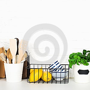 Kitchen table shelf with cutlery, spoons, spatulas, fresh basil, cutting boards, fresh vegetables, lemon on a simple