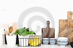 Kitchen table shelf with cutlery, spoons, spatulas, fresh basil, cutting boards, fresh vegetables, lemon on a simple