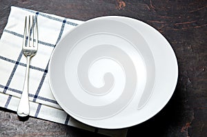 Kitchen table with towel, fork and white plate. Wooden table with a cloth napkin