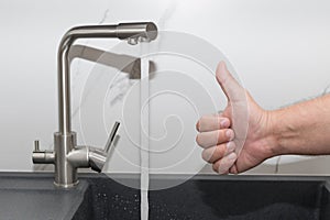 kitchen tap with flowing water. Man showing thumbs up