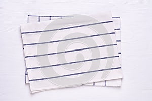 Kitchen towels with blue stripes on white wooden table top. Mock up for design