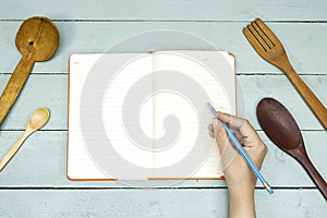 kitchen utensil with blank recipe book and woman hand holding a pencil