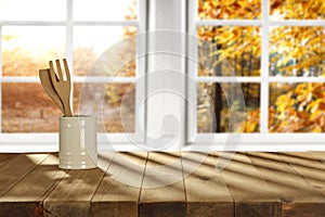 Kitchen utensil on wooden table top and blurred autumn window background in distance.