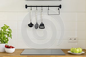 Kitchen utensils above wooden countertop with apples, tomatoes a